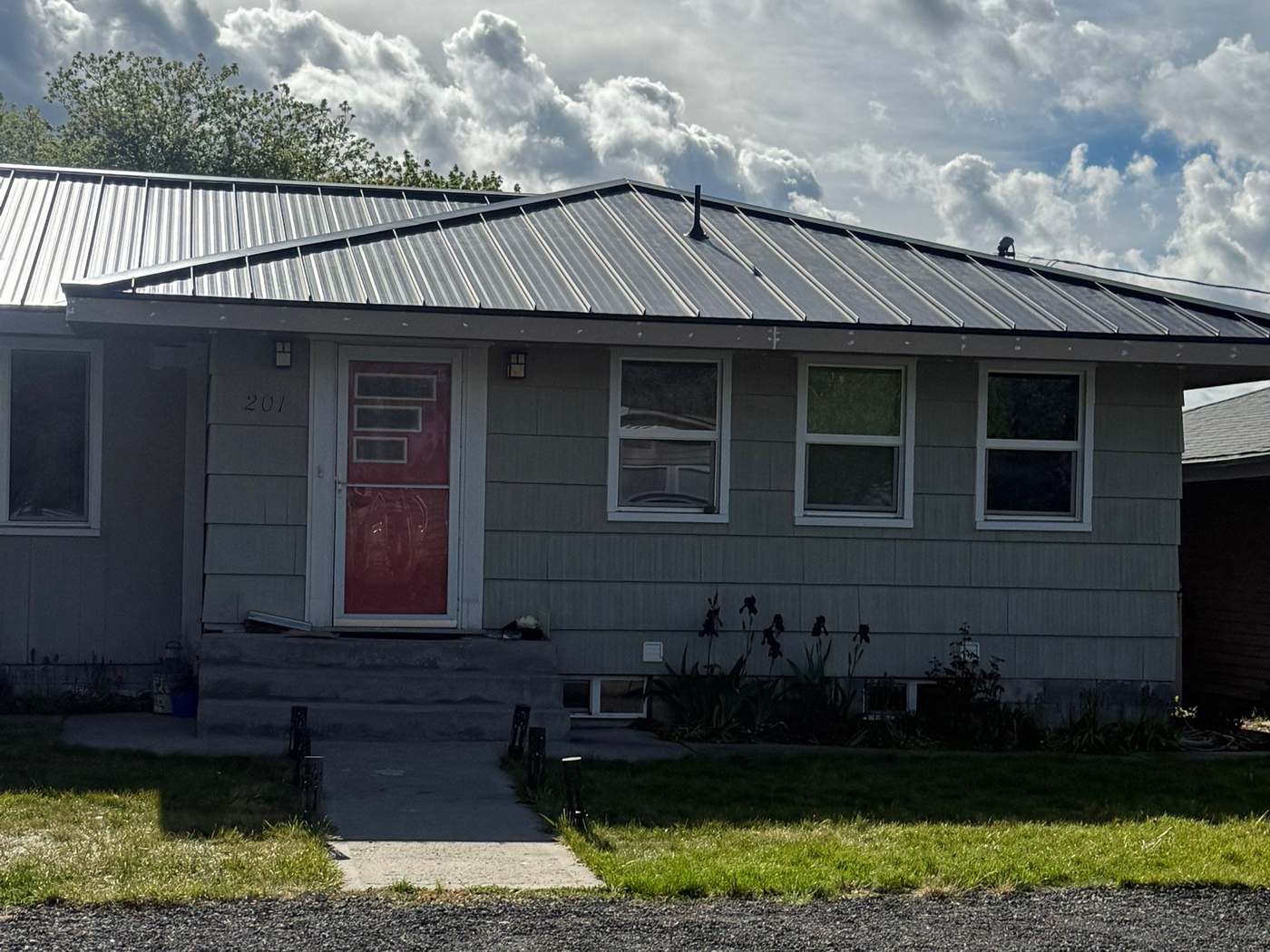 A clean gray standing-seam metal roof on a Pacific Northwest home under dramatic clouds — a completed Peaks & Valleys metal roof.