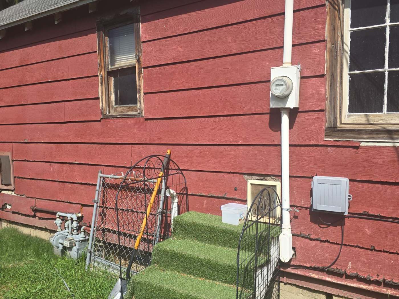 Faded, chalking red lap siding and bare, weathered window trim on an older home — the kind of failing exterior paint that has to be diagnosed and prepped before it's recoated.
