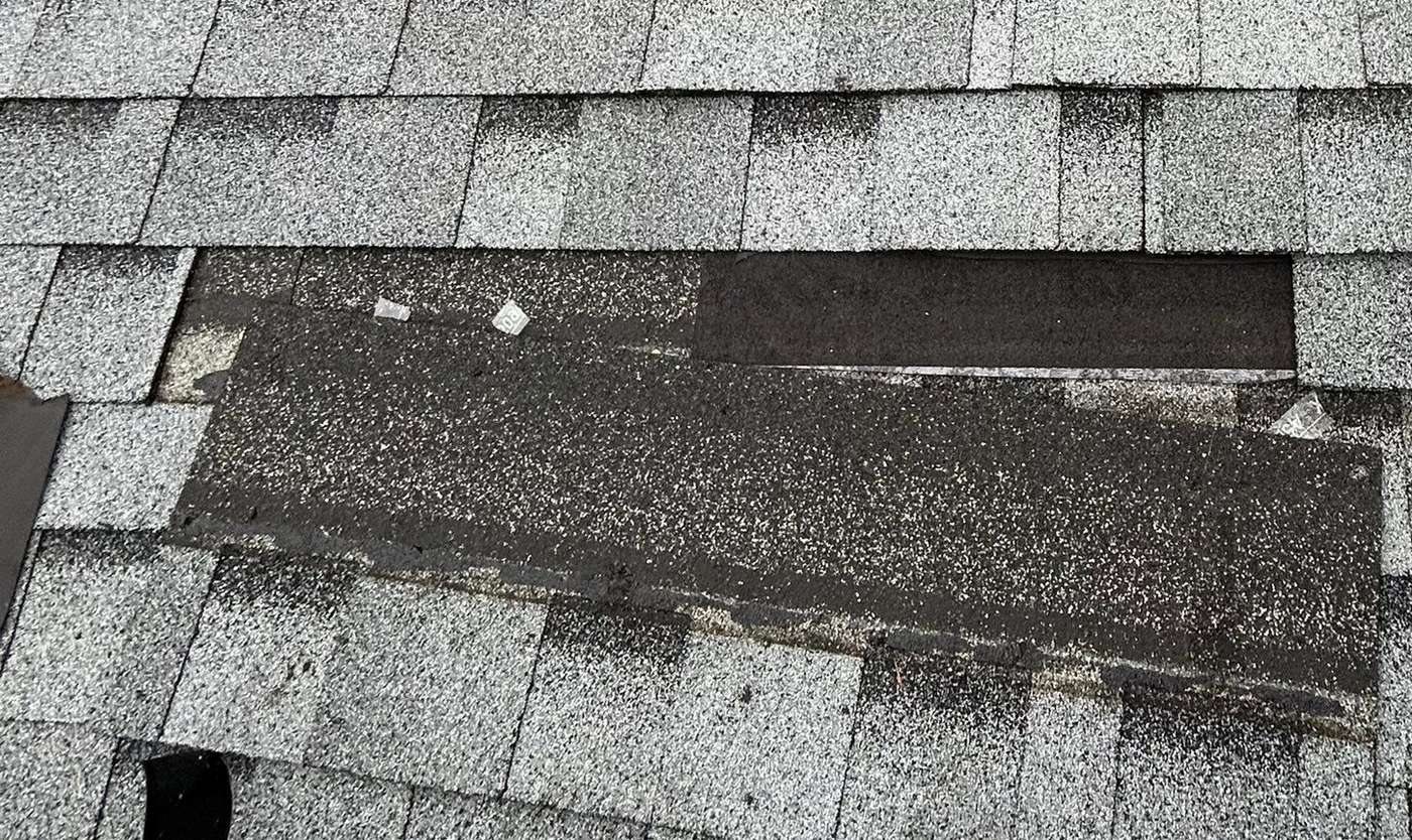 Missing shingle tab exposing worn underlayment on an asphalt roof